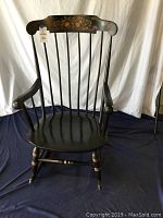 Full view of black wooden rocking chair showing spindled backrest, armrests, contoured seat, and base with rockers.