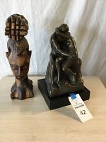 Two sculptures displayed side by side on a table against white background. Wooden carved woman bust on left and bronze couple sculpture on right.