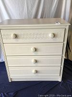 Front view of off white chest of drawers showing seashell shaped drawer knobs and carved seashell motif trim above top drawer
