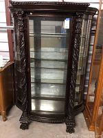 Full front view of carved wood curio cabinet showing curved glass door, twisted carved columns and claw feet