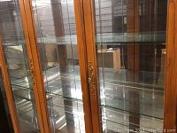 Front view showing beveled glass doors with brass hardware and 4 glass shelves inside the oak curio cabinet.