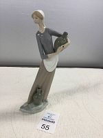 Porcelain figurine of a lady carrying a large jug with a smaller jug on the base near her feet, positioned on a table against a plain background.