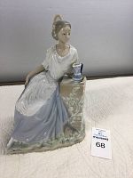 Photo of the Nao porcelain figurine showing woman in pastel dress resting on a column with floral decoration and jug.