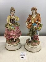 Front view of the pair of porcelain lamp bases showing a girl figurine on left and boy figurine on right, each holding flowers and standing on decorative bases.