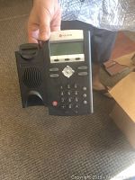 Polycom VVX 500 PoE desk phone held by hand showing keypad and display
