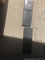 Two black wired Logitech keyboards placed on carpet, showing standard key layout, number pad, function keys, and USB connection cables.