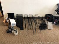 Assorted black desktop organizers and file folder sorters arranged on carpeted floor, including wire racks and stackable trays.