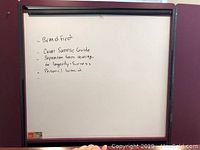 Whiteboard showing handwritten notes with black marker, mounted in dark frame with tray below.