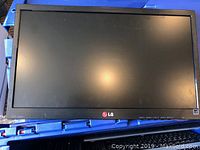 LG LED computer monitor with stand placed on blue plastic crate. Screen shows reflections, no power on screen.