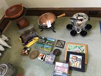 Wide view of lot items including copper fondue pot, decorative tiles, trivets, coasters, terracotta pot stand.