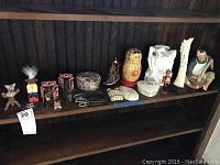Wide view of all collectibles arranged on a wooden shelf including nesting doll, carved pillars, figurines, decorative boxes, model ship, and other items.