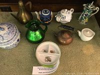 Assorted vintage teapots, pitchers, a kettle, and a serving dish on a carpeted floor.