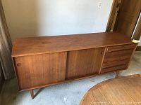Full view of teak credenza showing drawers and sliding doors on tapered legs