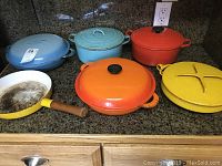 Overview photo showing all 6 cookware pieces including the frying pan, Dutch ovens, divided pan, and casserole in various colors on kitchen counter.