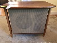 Front view of mid century modern wooden speaker cabinet with fabric cover showing large speaker cone shadow.