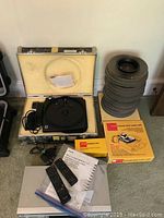 Kodak projector in case with six gray slide carousels stacked, Toshiba silver VHS/DVD player with two remotes and instruction manual in view.