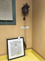 Overall view of cuckoo clock mounted on wall next to framed New York Times front page reproduction leaning against counter.