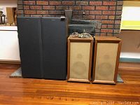 Four speakers against brick background and wood flooring: two modern Sony tall speakers with black fabric grilles on left, two vintage custom-made wooden speakers with light cloth fronts on right.