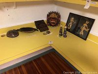 Overview of the Indonesian art items displayed on a yellow surface: wooden bowl, nut dish, carved panel, mask, figurines, and framed bamboo art
