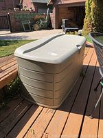 Side front view of the Rubbermaid outdoor storage chest showing its beige color, horizontal grooves, and lid shape.