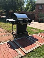 Full view of Brinkmann propane grill showing four burners, side shelves, wheels, and outdoor setting.