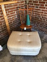 Wooden chair with spindle back, green mid-century modern lamp on the chair, and beige upholstered ottoman in front.