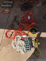Photo showing multiple orange and black extension cords coiled on floor along with white ropes and Belkin surge protector power strip