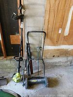 Ryobi grass trimmer and Yardworks manual push reel mower side by side in garage space.