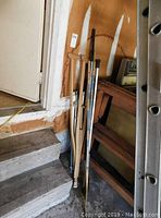 Photo showing three hockey sticks, a pair of crutches, and part of an easel leaning against a wall by stairs.
