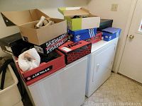 Photo of multiple shoe boxes stacked on top of washing machines, showing various brands and styles.