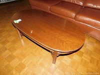 Full view of medium brown wood coffee table with rectangular shape and rounded corners in front of leather sofa.