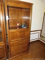 Front view of the wooden wall unit showing open shelf with items, drop-front compartment, and drawers.