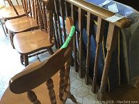 Photo of six assorted wood dining chairs showing four chairs without arms aligned, two chairs with armrests leaning against a railing