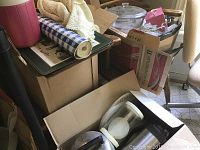 Three boxes packed with kitchenware and other items including a roll of shelf liner, assorted kitchen utensils and containers, and some cardboard boxes.
