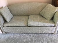 Full view of light green fabric sofa bed with two cushions, showing overall condition and wear.