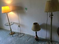 Photo showing three lamps against a wall: one tall floor lamp with glass side tray, one medium floor lamp, and one short table lamp.