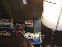 Photo showing the floor lamp, rolling table and assorted books stacked on top against a wooden wall.