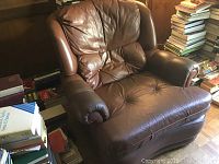 Brown leather Sklar Pepplar recliner chair in a room by stacks of books, showing overall shape and condition.
