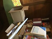 Photo showing two ironing boards, cardboard boxes filled with books, including an economics textbook and assorted volumes.