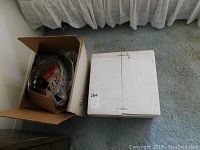 Two boxes on carpet: one open showing contents of an electric fry pan, other sealed white box