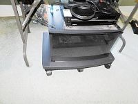 Black TV stand with glass front lower compartment and Sony VCR on top, from front angle showing casters.