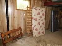 Wooden bed frame parts with headboard and footboard, mattresses leaning on frame parts in basement environment