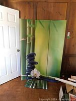 Three-panel green room divider with bamboo stalks, stone stack, and orchid flower design leaning against wood-paneled wall