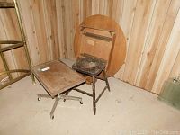 Three tables in basement corner: faux wood chrome caster table, a chair converted to plant stand, and round Rock Maple table without legs attached.