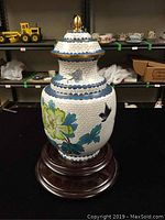 Full view of the cloisonne ginger jar with lid on a wooden stand showing floral and bird designs
