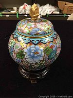 Front view of cloisonne ginger jar with lid on wooden stand showing floral pattern and gold ornamental lid handle