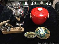 Full view of vintage barware lot on black cloth, including chrome cocktail shaker, red Thermos ice bucket, stag horn bar implements on wood base, and signed Jules Perrier dish and lighter.