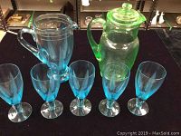 Blue glass pitcher with five matching blue glasses arranged on table.