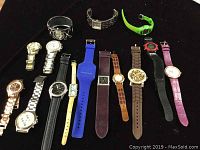 Full lot of 15 quartz wristwatches displayed on black background showing diversity of straps, faces, colors, and styles.
