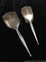 Photo displaying the vintage sterling silver hand mirror and matching brush set from the front and back showing shield-shaped silver backplates and tapered handles.